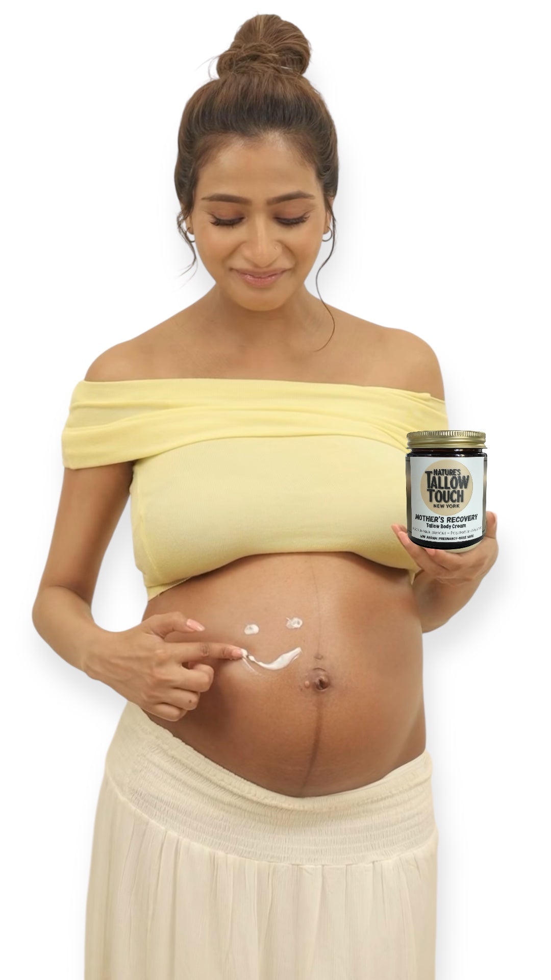Pregnant woman applying Mother’s Recovery Tallow Body Cream to her belly while holding the jar, on a clean white background.